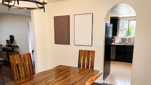 A dining area with a wooden table and chairs, a kitchen in the background, and two framed artworks on the wall. - Movie Theater Retreat With Pickleball Court (Post Falls)