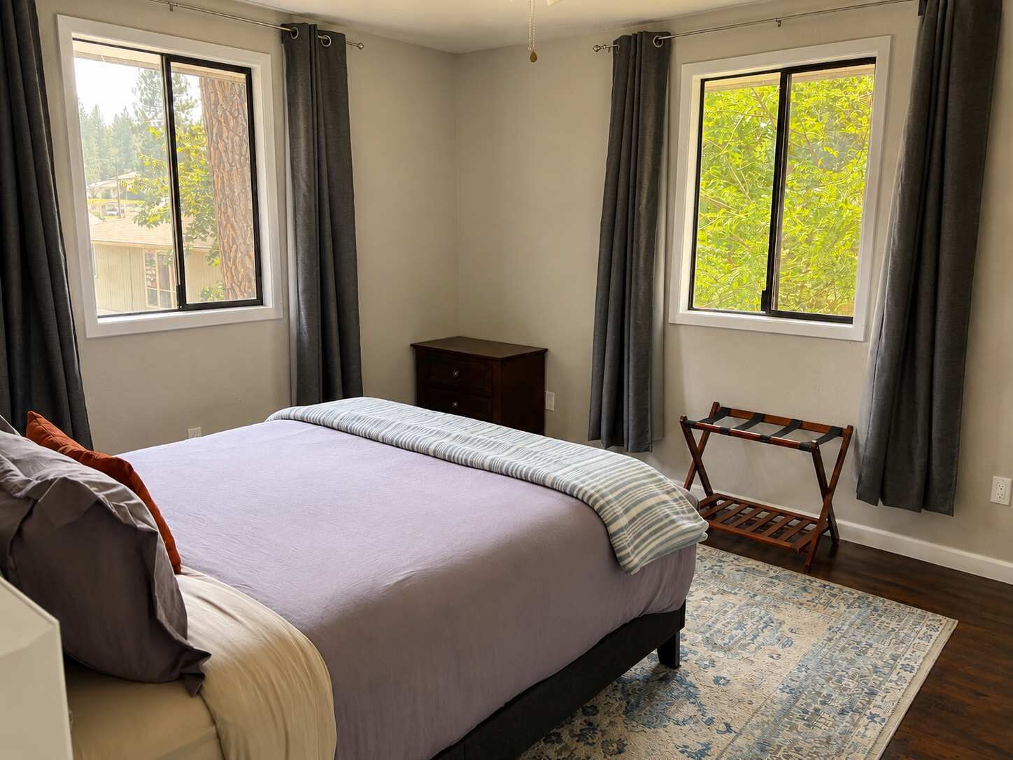 Une chambre à coucher avec un lit, une table de chevet, une chaise et deux fenêtres avec des rideaux.