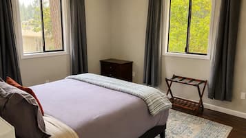 Une chambre à coucher avec un lit, une table de chevet, une chaise et deux fenêtres avec des rideaux.