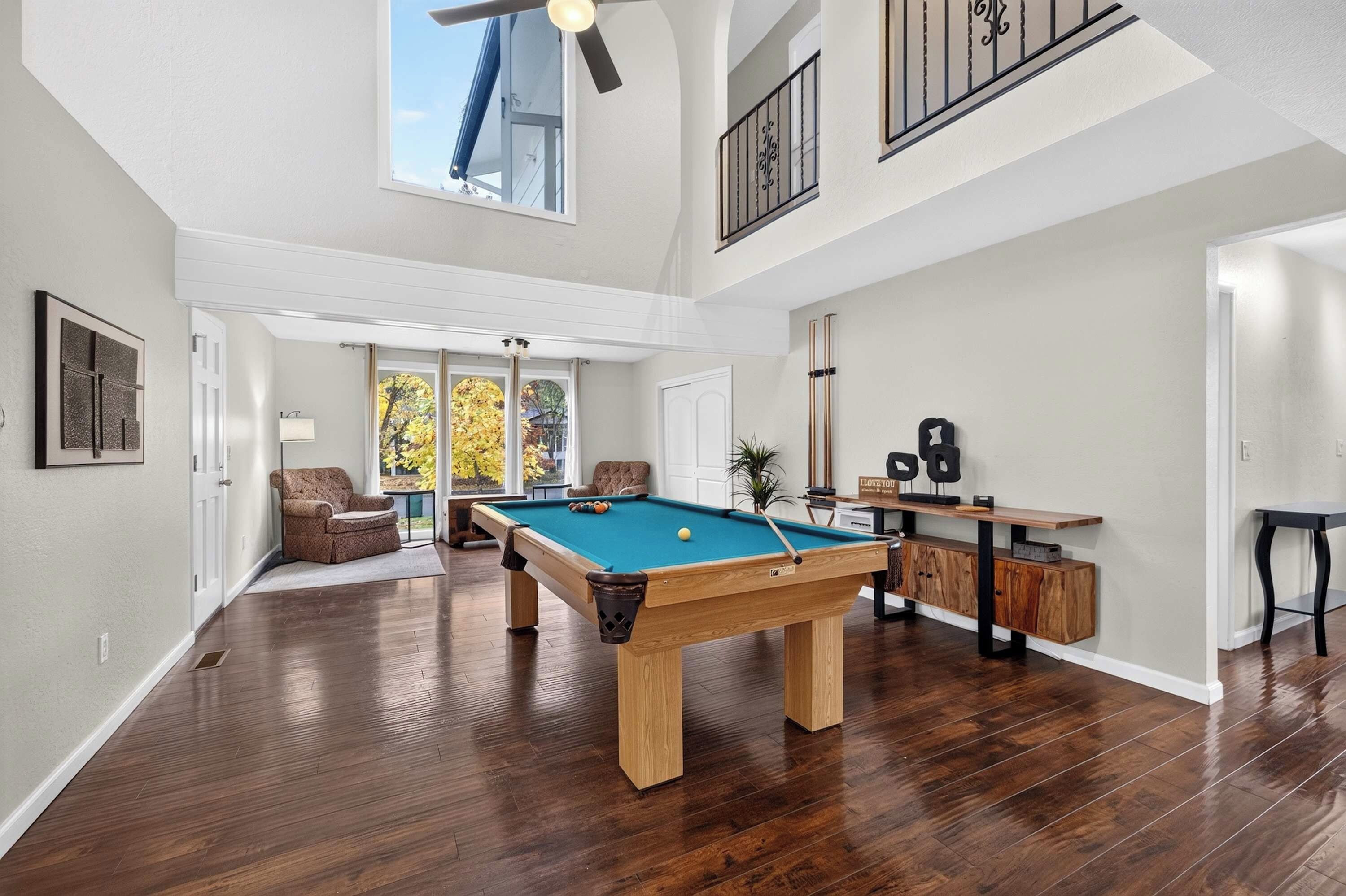 Une pièce spacieuse équipée d’une table de billard, d’un ventilateur de plafond et offrant une vue sur l’extérieur.