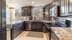 A modern kitchen with dark cabinetry, stainless steel appliances, and a granite countertop. - Movie Theater Retreat With Pickleball Court (Post Falls)
