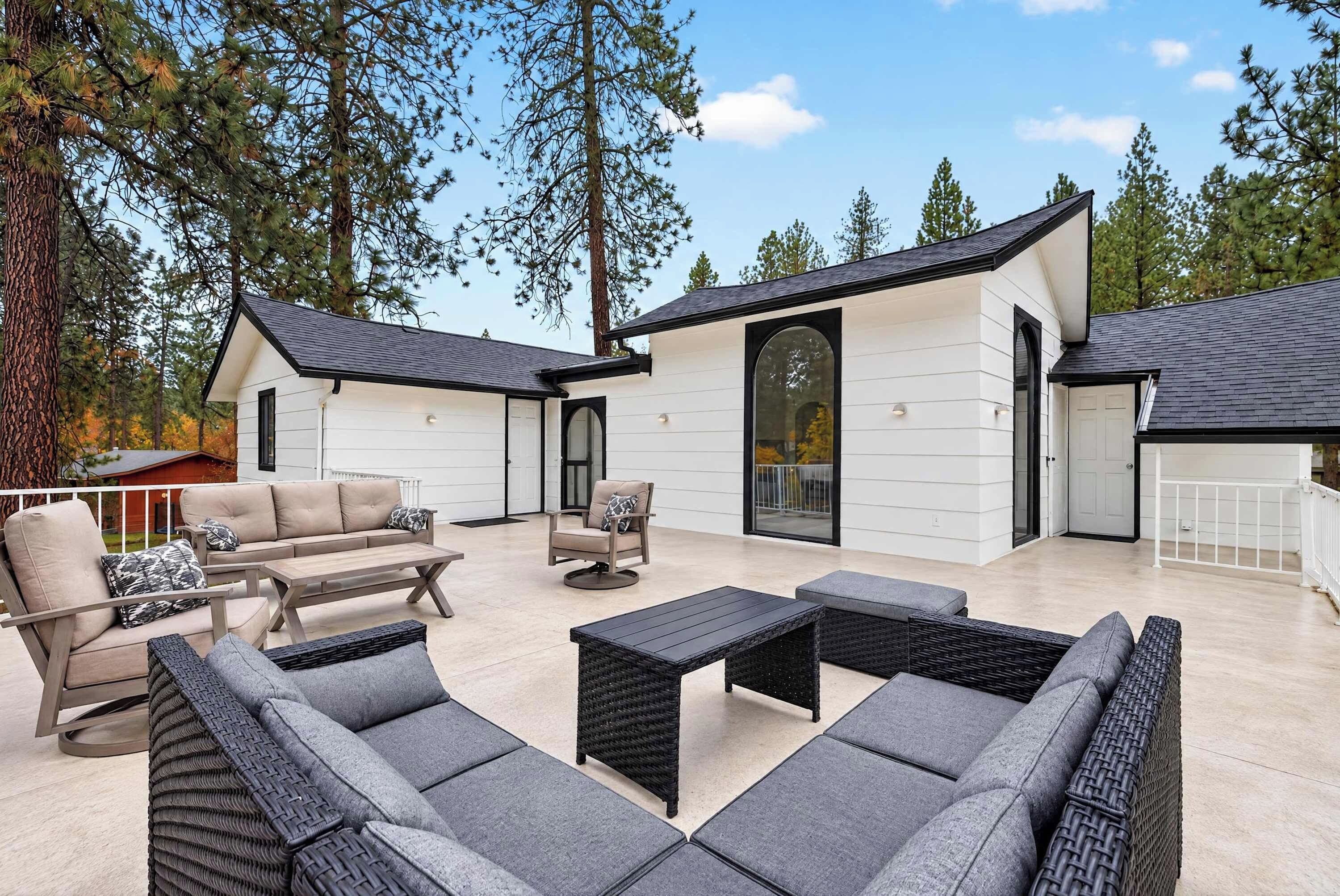 A modern outdoor living space with a patio, seating, and a large window overlooking a forested area.