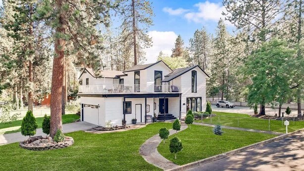 A two-story house with a balcony, surrounded by a well-maintained lawn and tall trees. - Movie Theater Retreat With Pickleball Court (Post Falls)