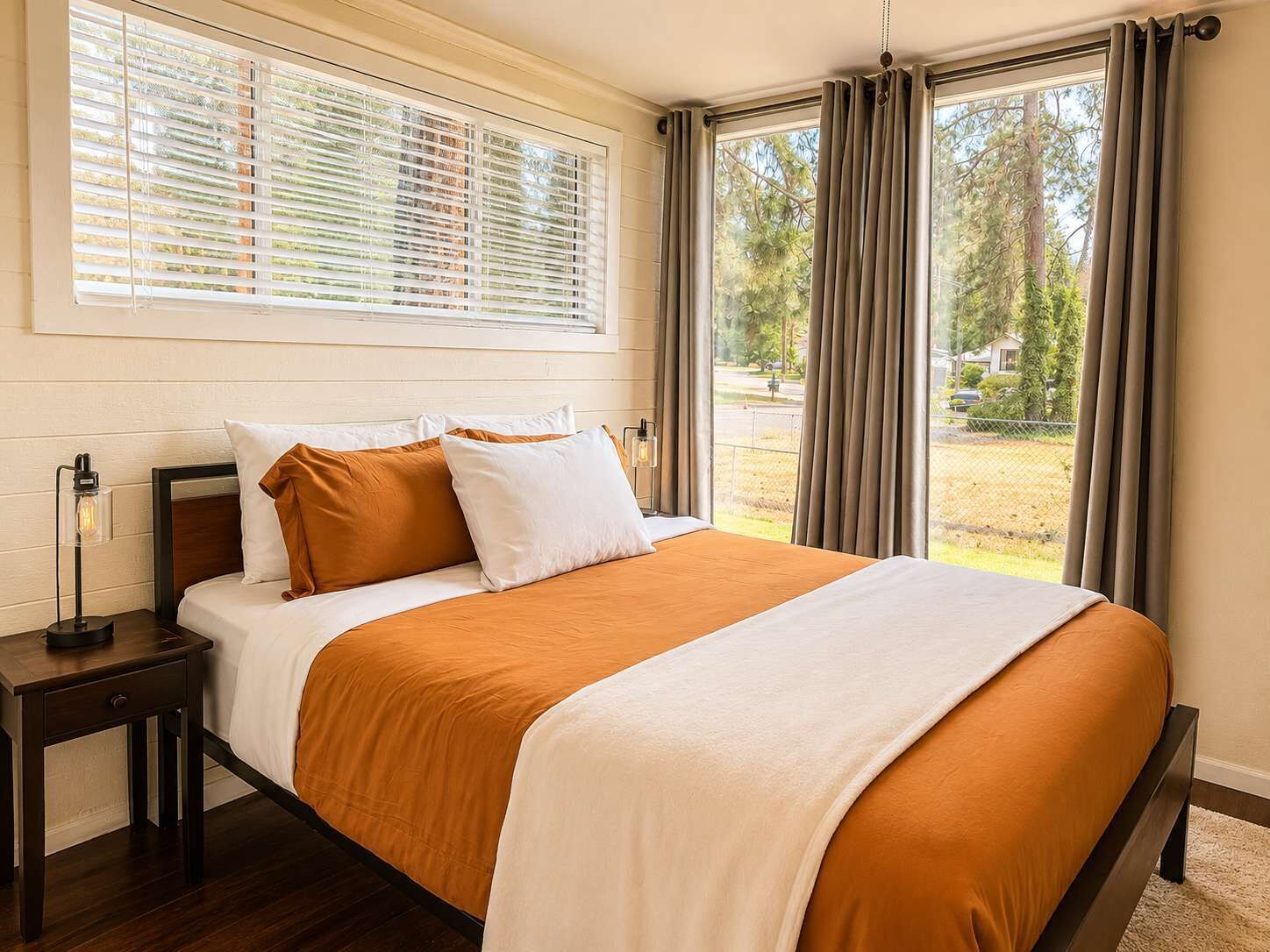 A bedroom with a large bed, a bedside table with a lamp, and a window with curtains.