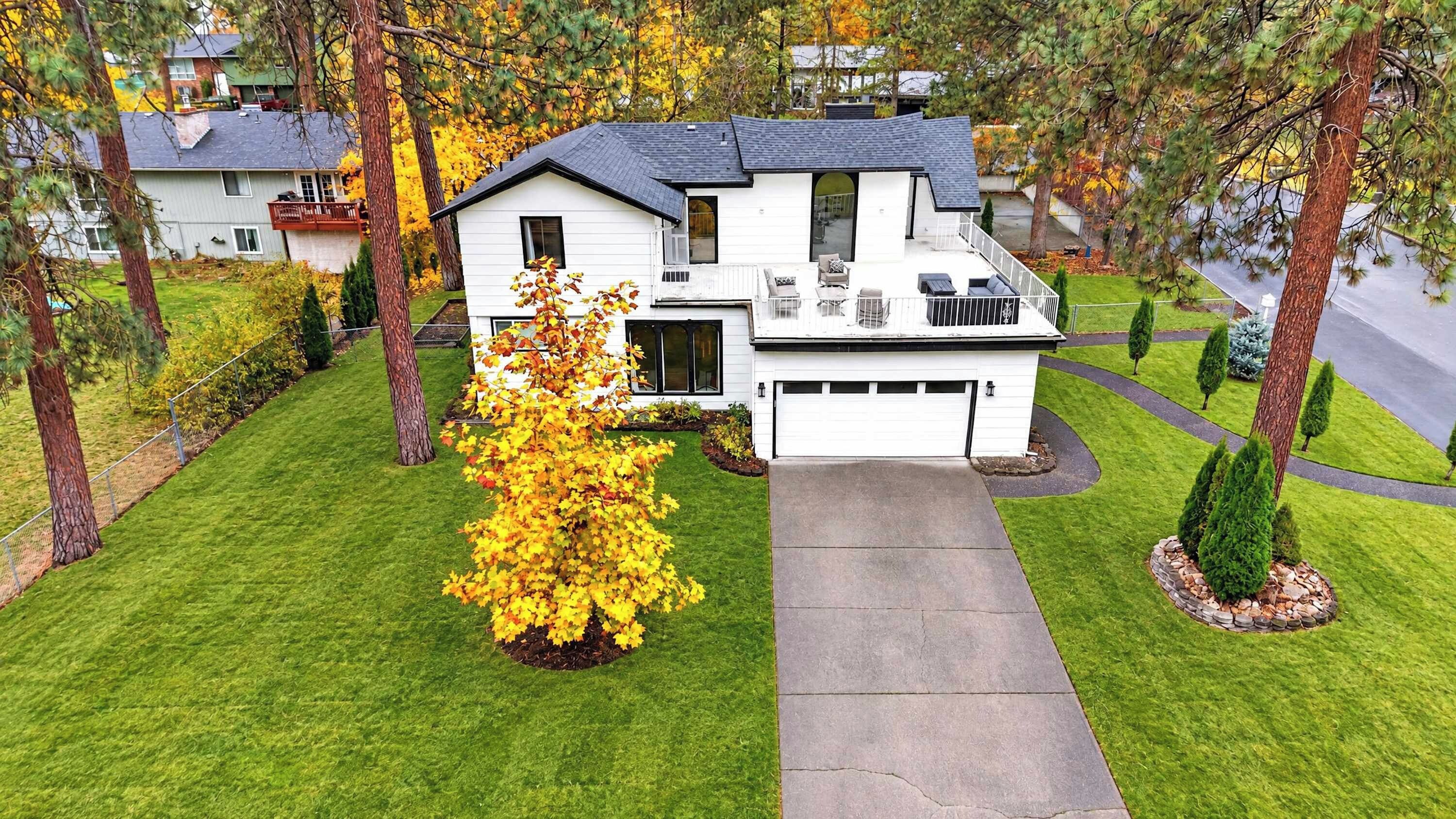 Une maison à deux étages avec un garage, une cour avant avec une pelouse et un arbre aux feuilles jaunes.
