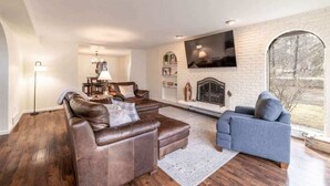 A living room with a fireplace, two sofas, a dining area, and a large window. - Movie Theater Retreat With Pickleball Court (Post Falls)