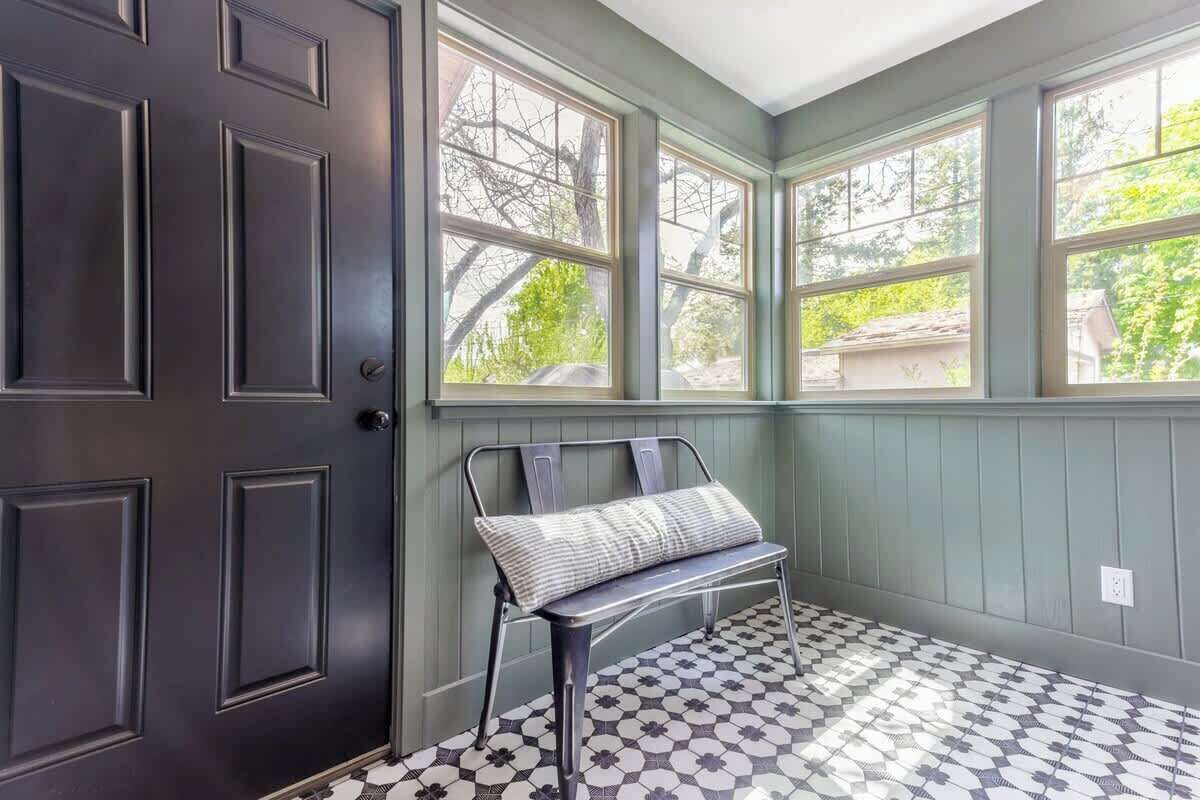 A room with a dark door, a bench with a cushion, and a window with a view of trees.