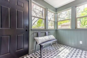 A room with a dark door, a bench with a cushion, and a window with a view of trees.