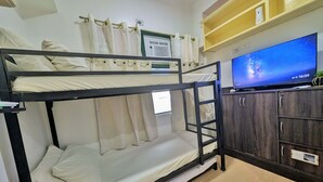 Kerrossängyllä varustettu huone, jossa on televisio, puukaapit ja ikkuna, jossa on verhot.