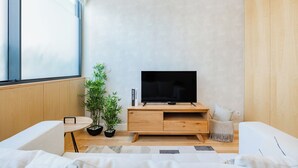 A modern living room with a flat-screen TV on a wooden TV stand, a small round table with a potted plant, and a white sofa. - Casa da Música Modern Flat (Porto)