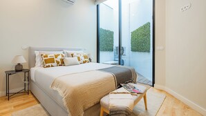 A modern bedroom with a large bed, bedside table, and a view of the outdoors through a sliding glass door. - Casa da Música Modern Flat (Porto)