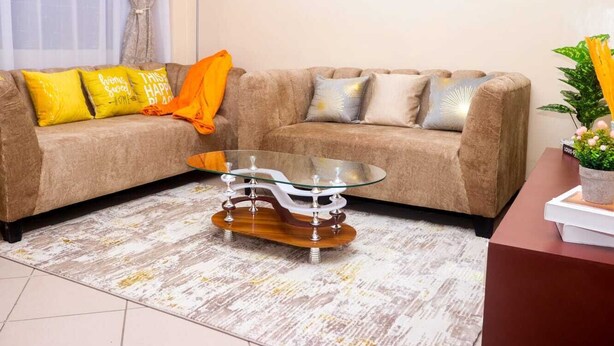 A living room with a beige sofa, glass coffee table, and a small side table with a plant.