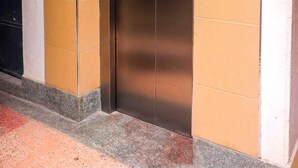 An elevator with a metallic finish, adjacent to a wall with orange tiles and a white baseboard.