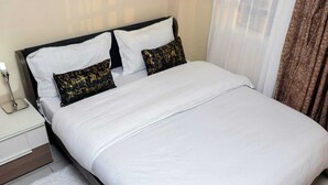 A neatly made bed with white linens and two decorative pillows, a bedside table with a lamp, and a white fluffy rug.