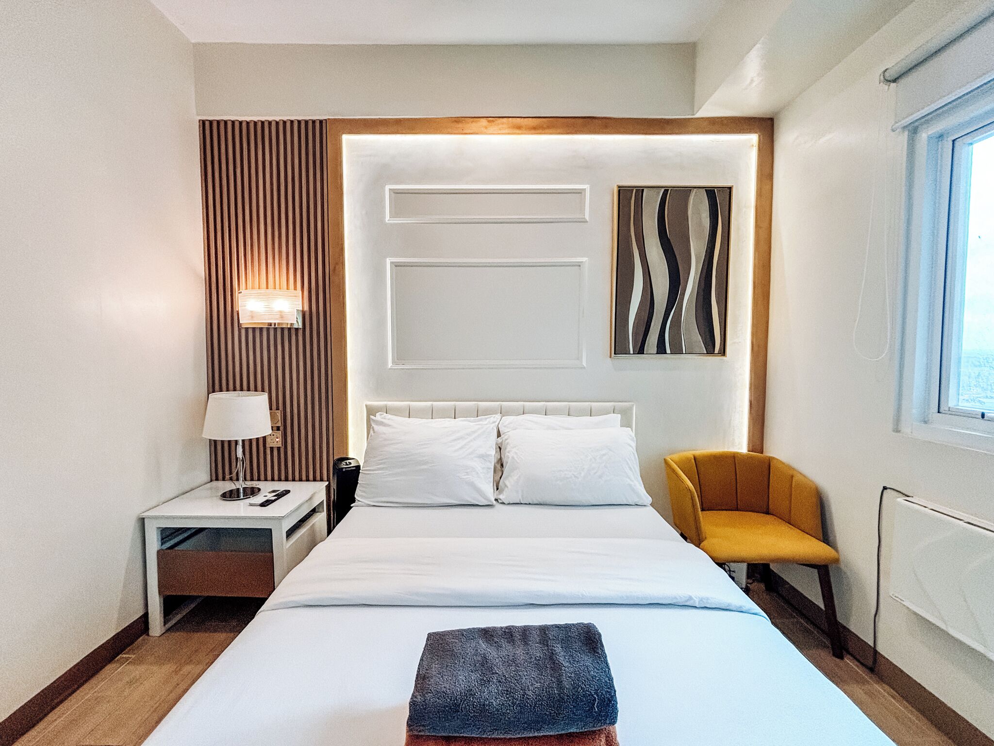 Une chambre d’hôtel avec un lit, une table de chevet, une lampe, une chaise et une fenêtre.