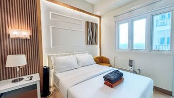 Una habitación de hotel con una cama, una mesita de noche con lámpara, una silla y una ventana con vistas.