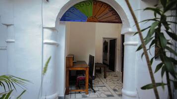 Uma porta em arco dá acesso a um espaço com soalho em azulejos e uma mesa de madeira.