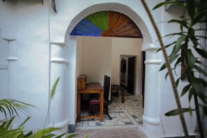 Uma porta em arco dá acesso a um espaço com soalho em azulejos e uma mesa de madeira.