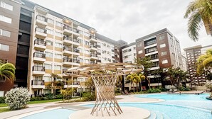 A swimming pool surrounded by multi-story residential buildings with balconies, a palm tree, and a wooden structure in the center. - Sunset Dreams Studio Haven (Iloilo City)