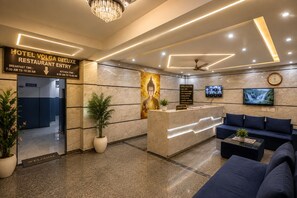 A hotel lobby with a reception desk, seating area, and a Buddha statue. - Hotel Volga Deluxe (New Delhi)