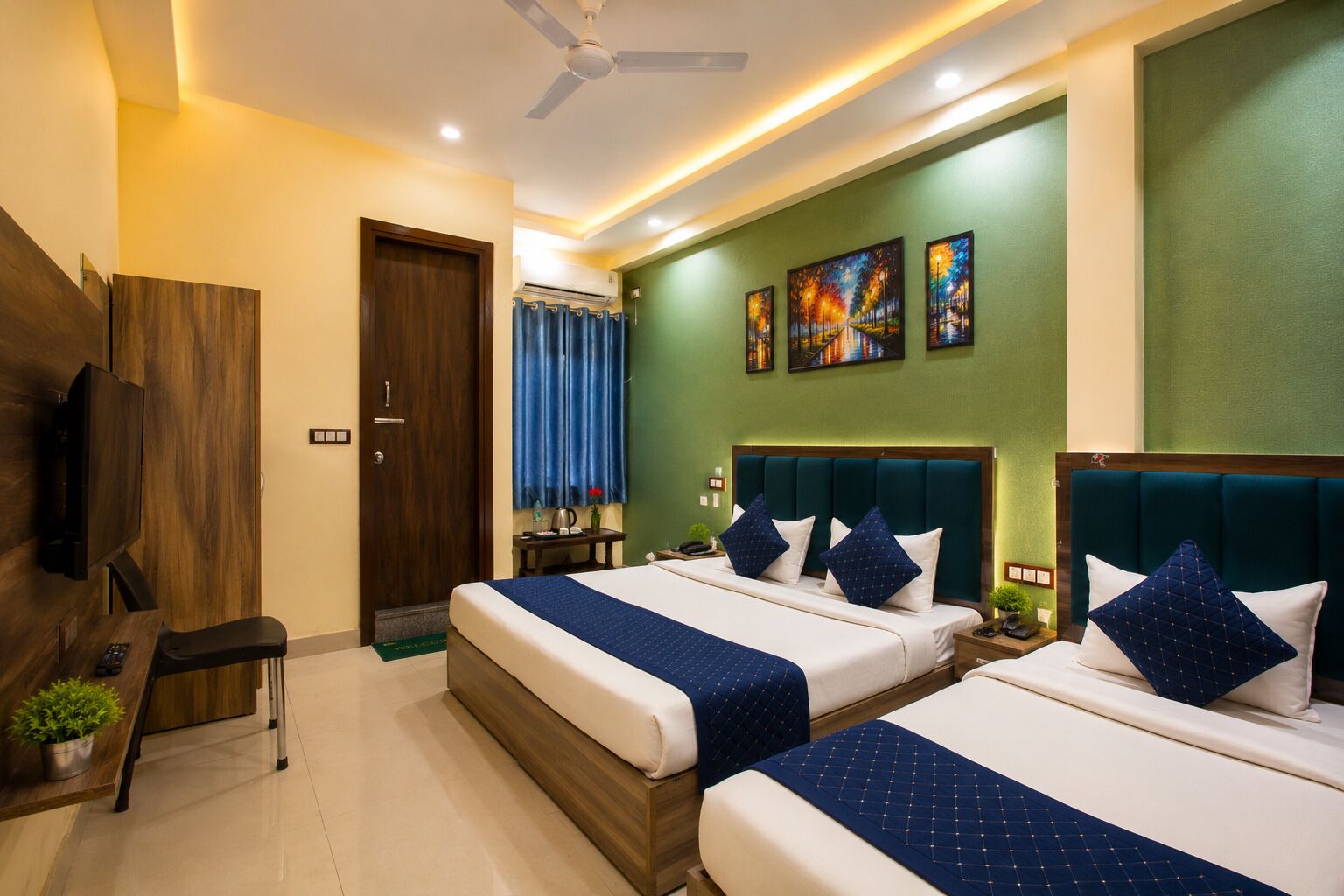 A hotel room with two beds, a TV, a desk, and a window with curtains.