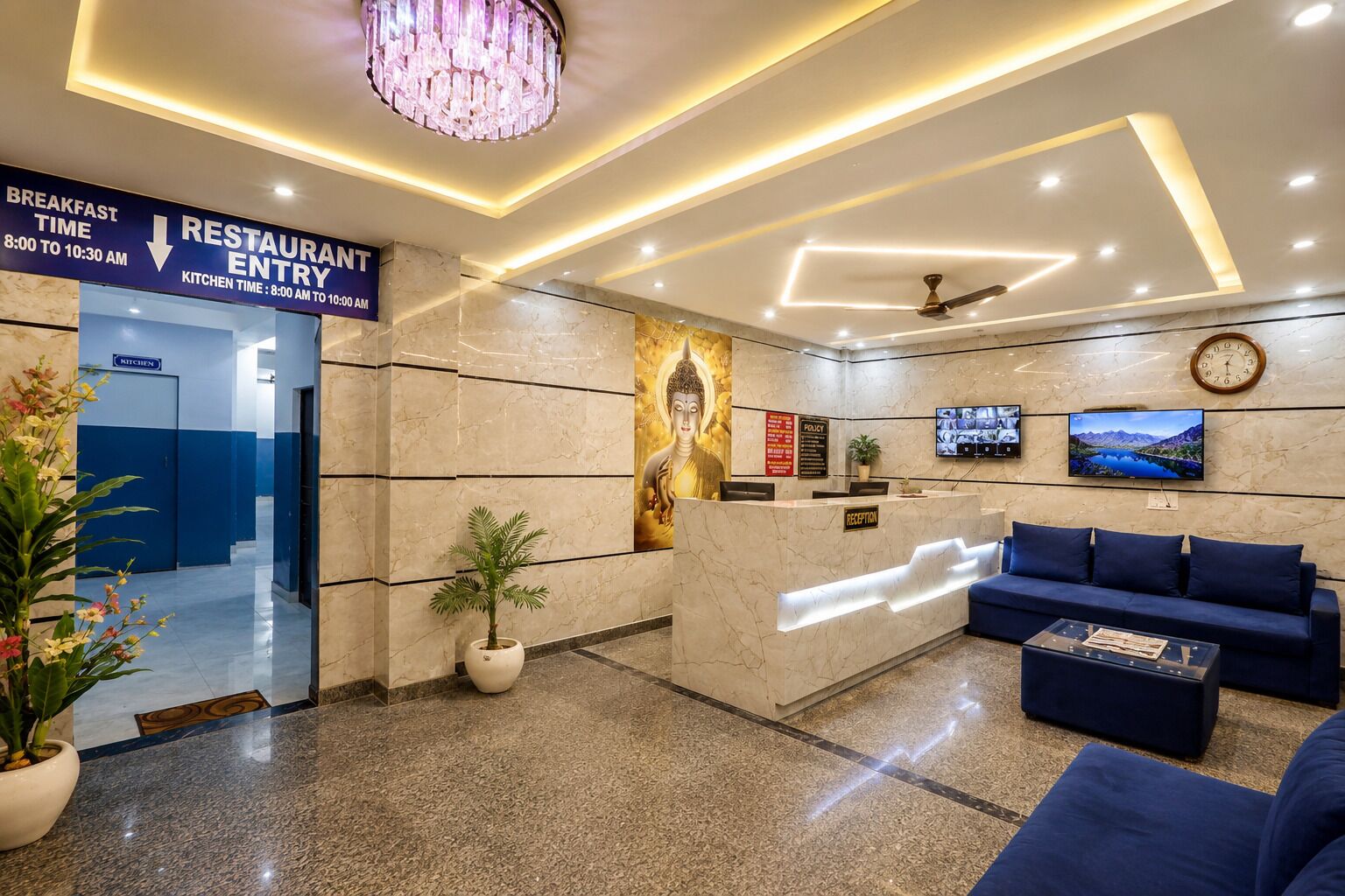 A hotel lobby with a reception desk, a blue sofa, a chandelier, and a clock on the wall.