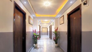A hotel hallway with wooden doors, potted plants, and framed pictures on the walls. - Hotel Volga Deluxe (New Delhi)