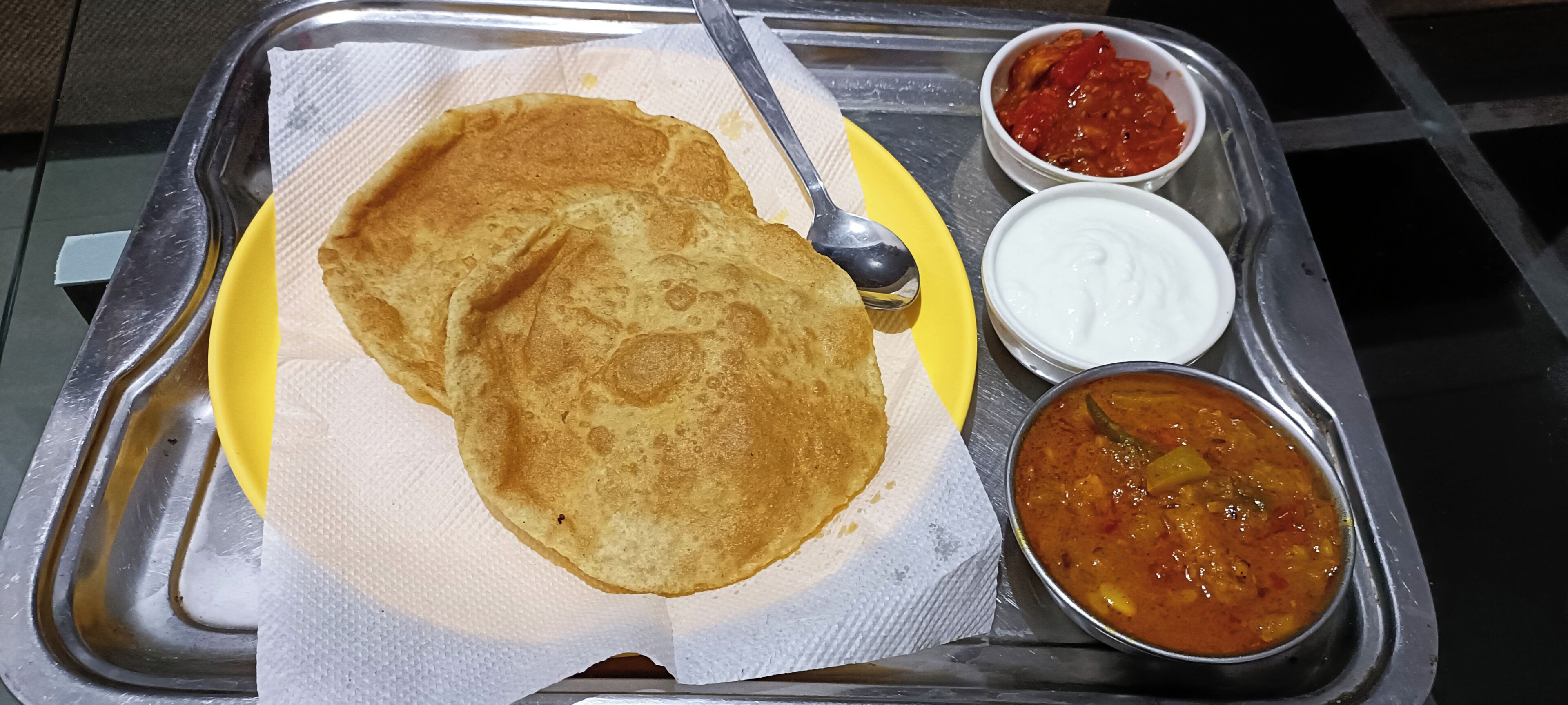 A meal with a folded flatbread, a spoon, and two small bowls of sauce on a metal tray.