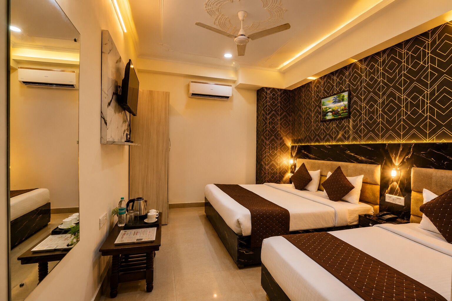 A hotel room with two beds, a desk with a chair, a TV mounted on the wall, and a ceiling fan.