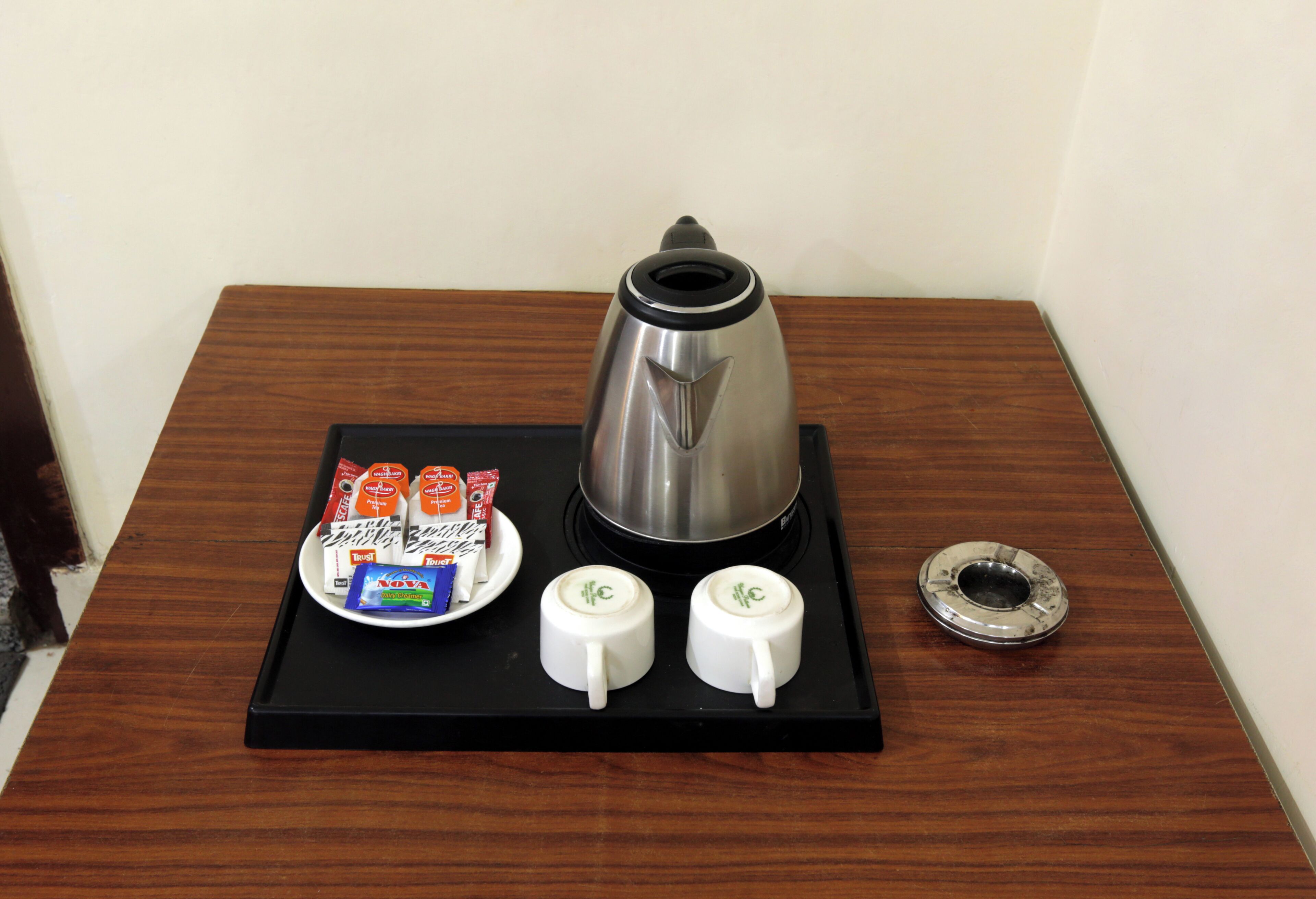 A coffee station with a coffee pot, two cups, and a tray with coffee packets and a spoon.