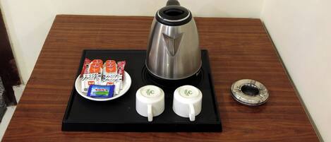 A coffee station with a coffee pot, two cups, and a tray with coffee packets and a spoon.