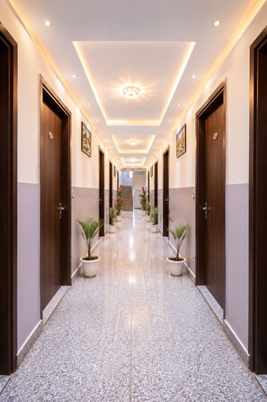 A hotel hallway with a polished marble floor, wooden doors, and potted plants. - Hotel Volga Deluxe (New Delhi)