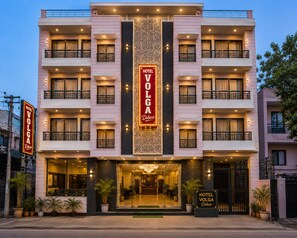 A multi-story hotel with balconies, a central decorative panel, and a well-lit entrance. - Hotel Volga Deluxe (New Delhi)