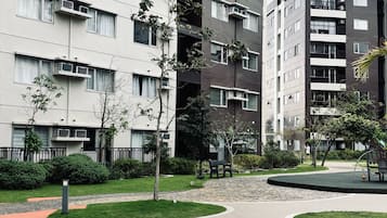 A modern apartment building with multiple balconies, a landscaped courtyard, and a paved walkway.