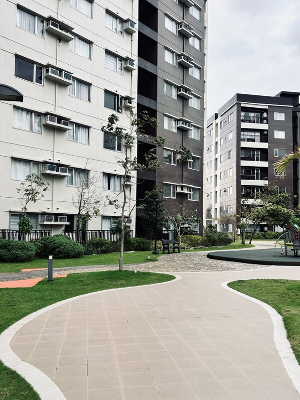 A modern apartment building with multiple balconies, a landscaped courtyard, and a paved walkway.