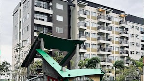 A playground with a green and red play structure, surrounded by a playground area with a pool and a multi-story residential building in the background. - The Sleek & Chic Hideaway (Iloilo City)