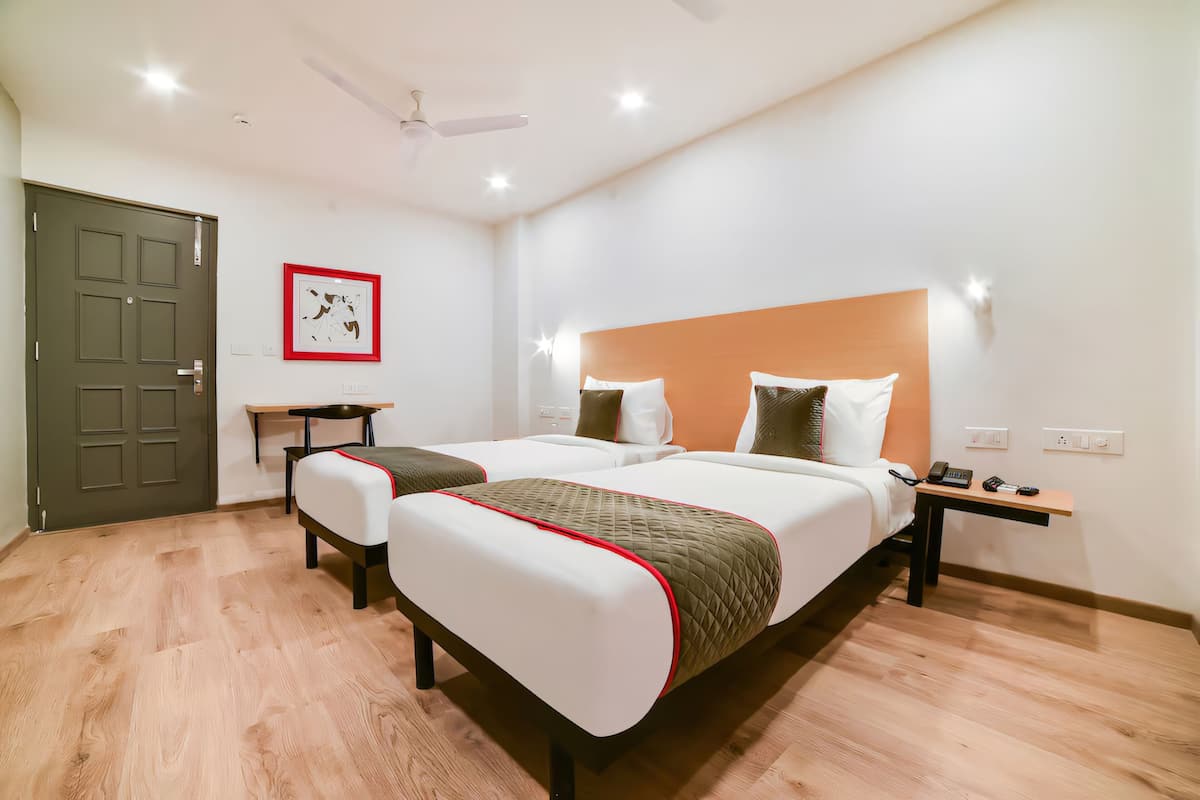 Quarto de hotel com cama de casal, mesas de cabeceira, escrivaninha, ventoinha no teto e uma porta.