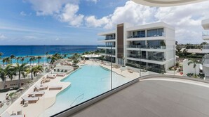 A modern hotel with a pool, palm trees, and a view of the ocean.