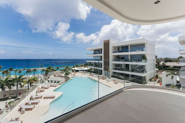 A modern hotel with a pool, palm trees, and a view of the ocean.