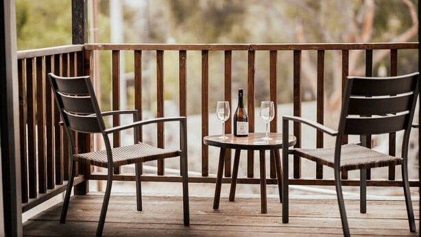 A wooden deck with two chairs and a small table, two wine glasses, and a bottle.