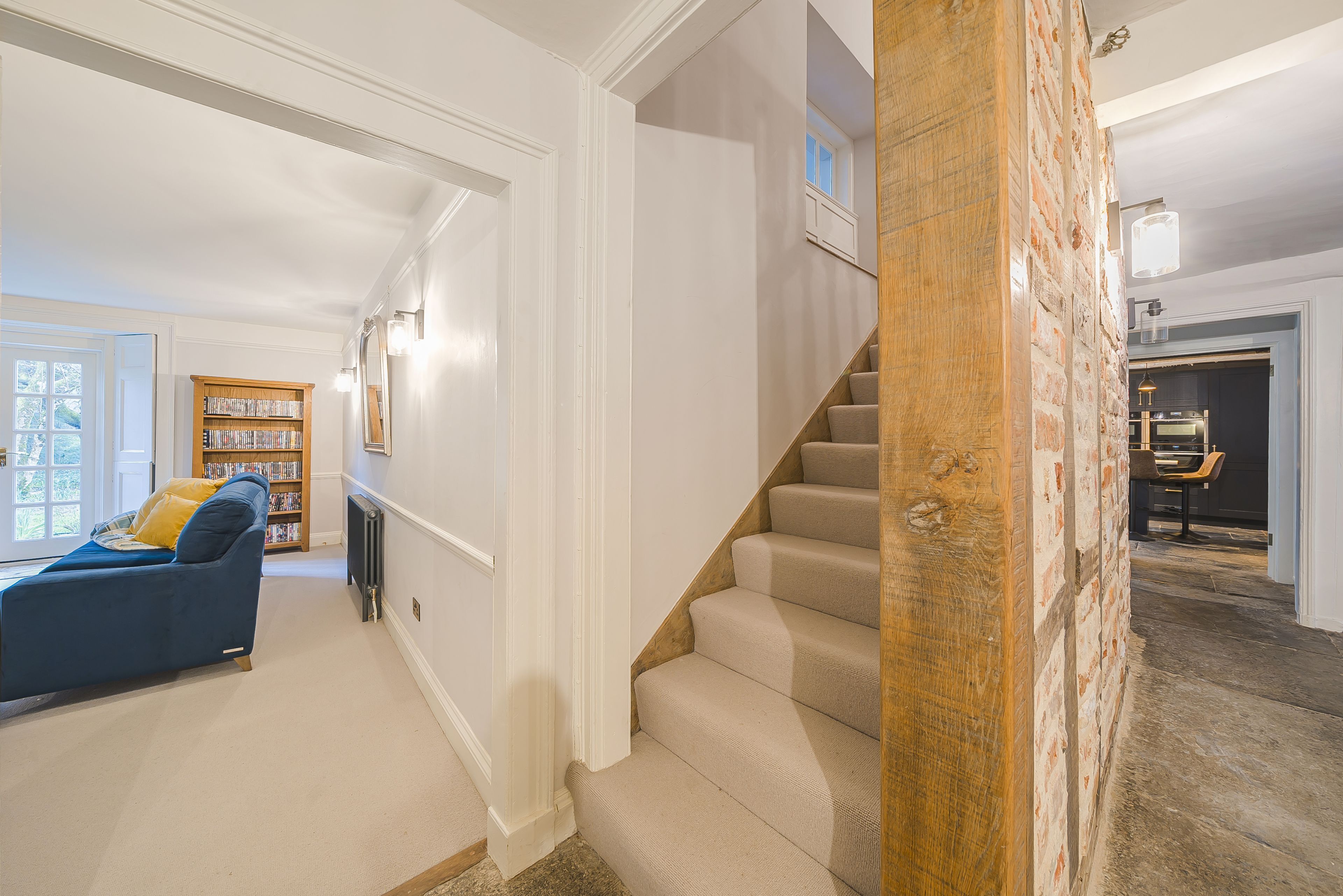 Un escalier dont les marches sont recouvertes d’une moquette beige et qui possède une rampe en bois, menant à une pièce au plancher foncé.