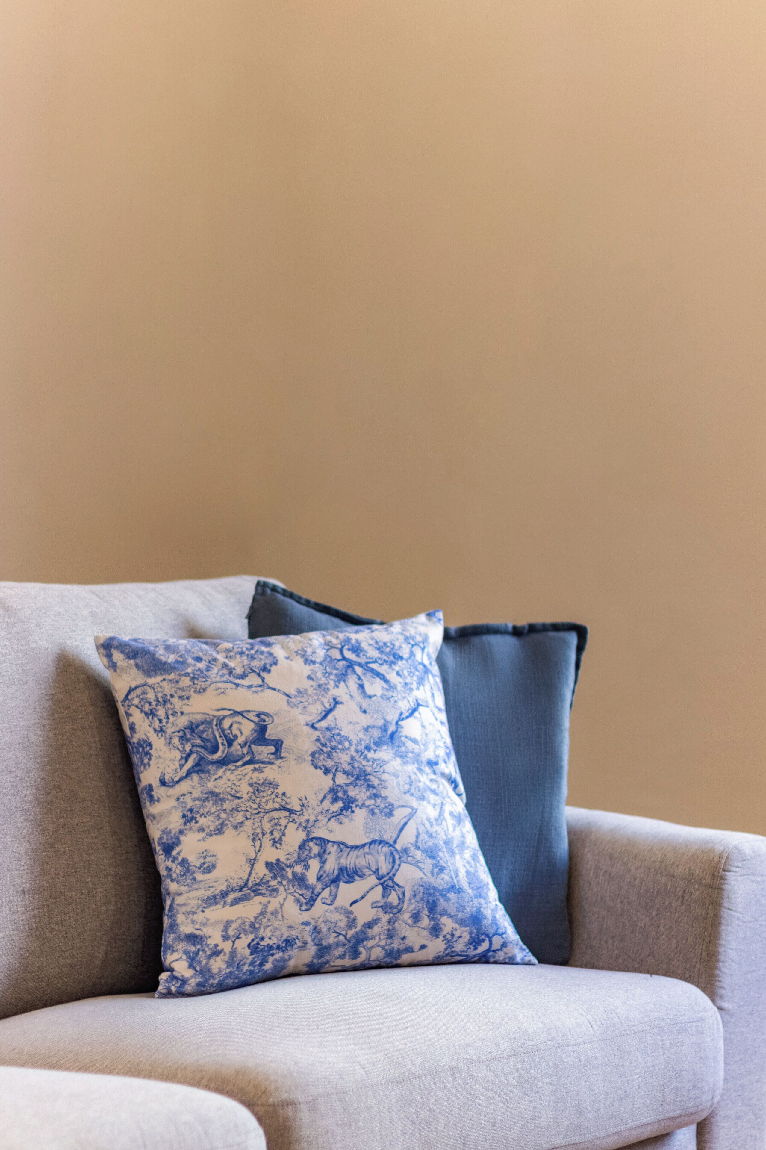 A sofa with a blue patterned pillow and a plain blue pillow against a beige wall.