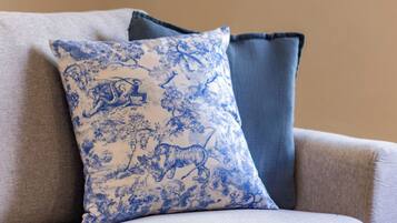 A sofa with a blue patterned pillow and a plain blue pillow against a beige wall.