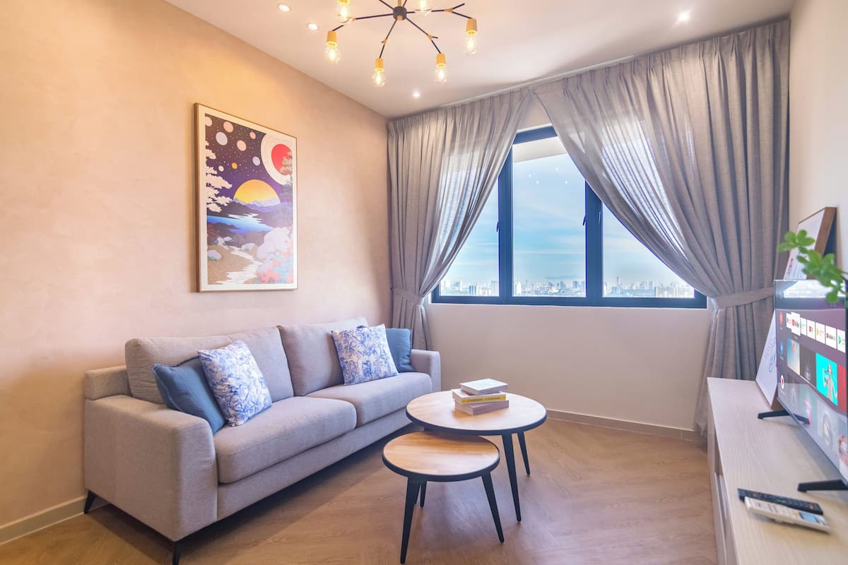 Ein modernes Wohnzimmer mit einer Couch, zwei kleinen Tischen, einem Fernseher und einem großen Fenster mit Vorhängen.