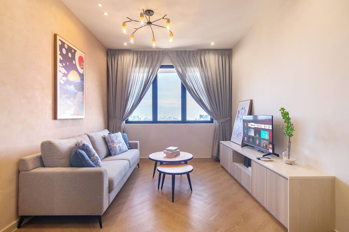 Ein modernes Wohnzimmer mit einer Couch, zwei runden Tischen, einem Fernseher und Blick auf die Stadt durch große Fenster.