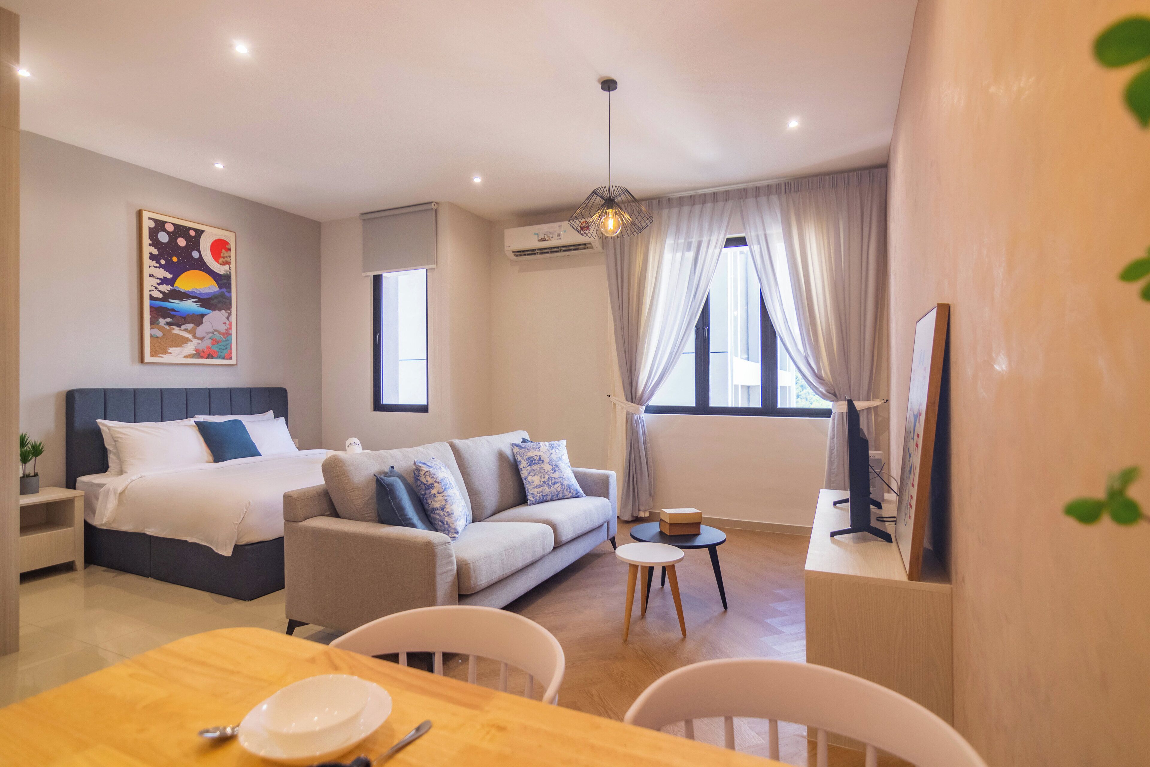 Quarto de hotel moderno com cama, sofá, mesa de jantar e televisão.