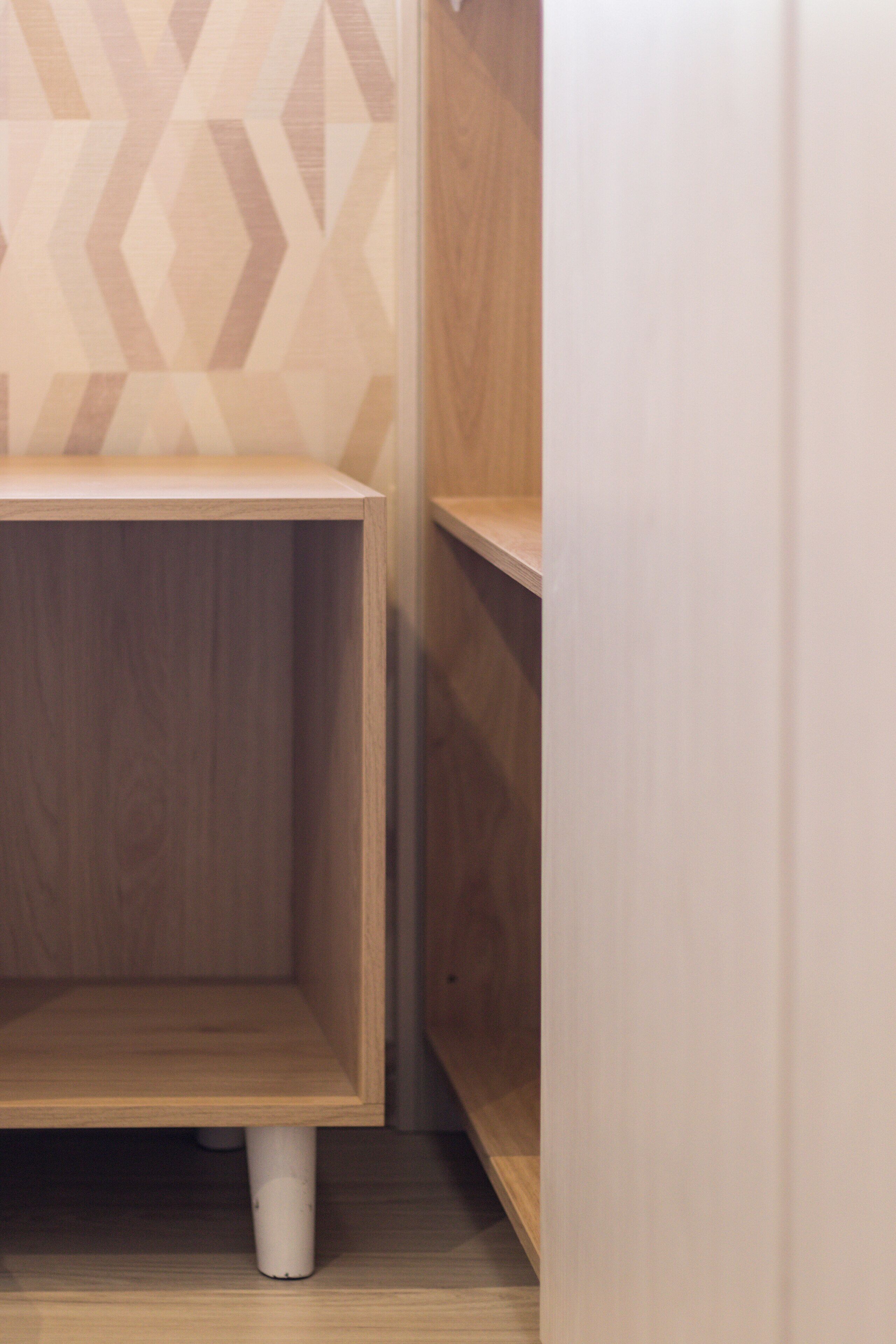A corner of a room with a wooden cabinet and a white wall with a geometric pattern.