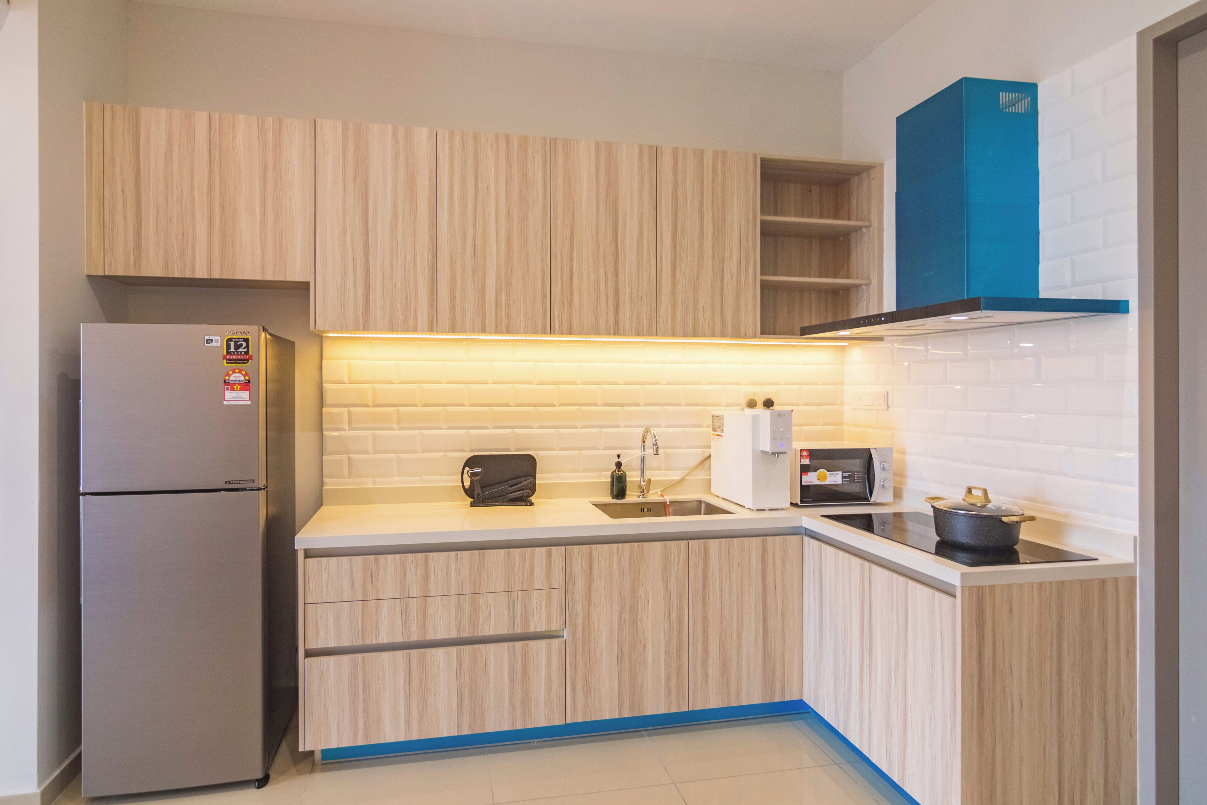A compact kitchen with light wood cabinets, a stainless steel refrigerator, a microwave, and a stove.