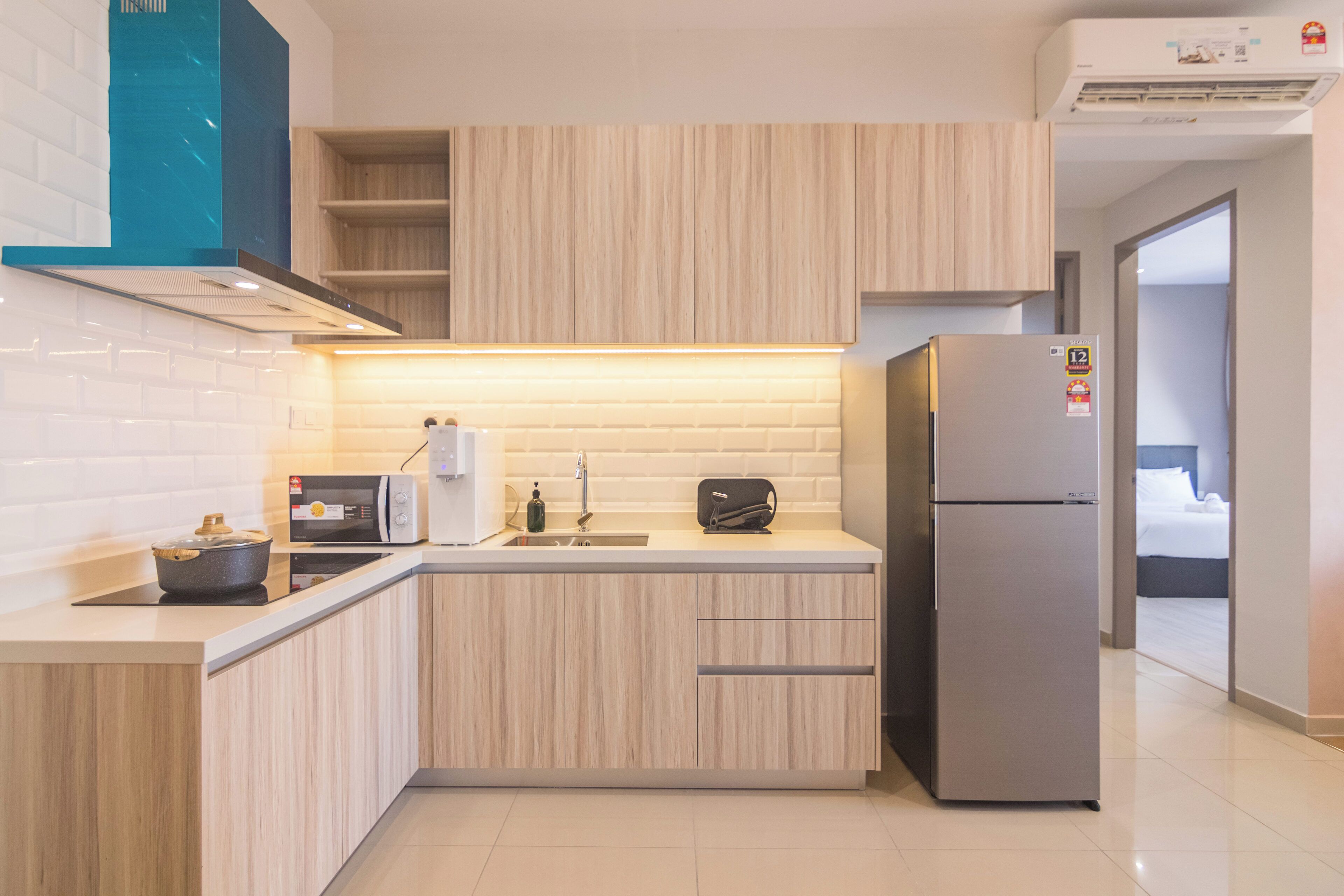 Una cocina moderna con alacenas de madera clara, un refrigerador de acero inoxidable, un microondas y un horno empotrado.