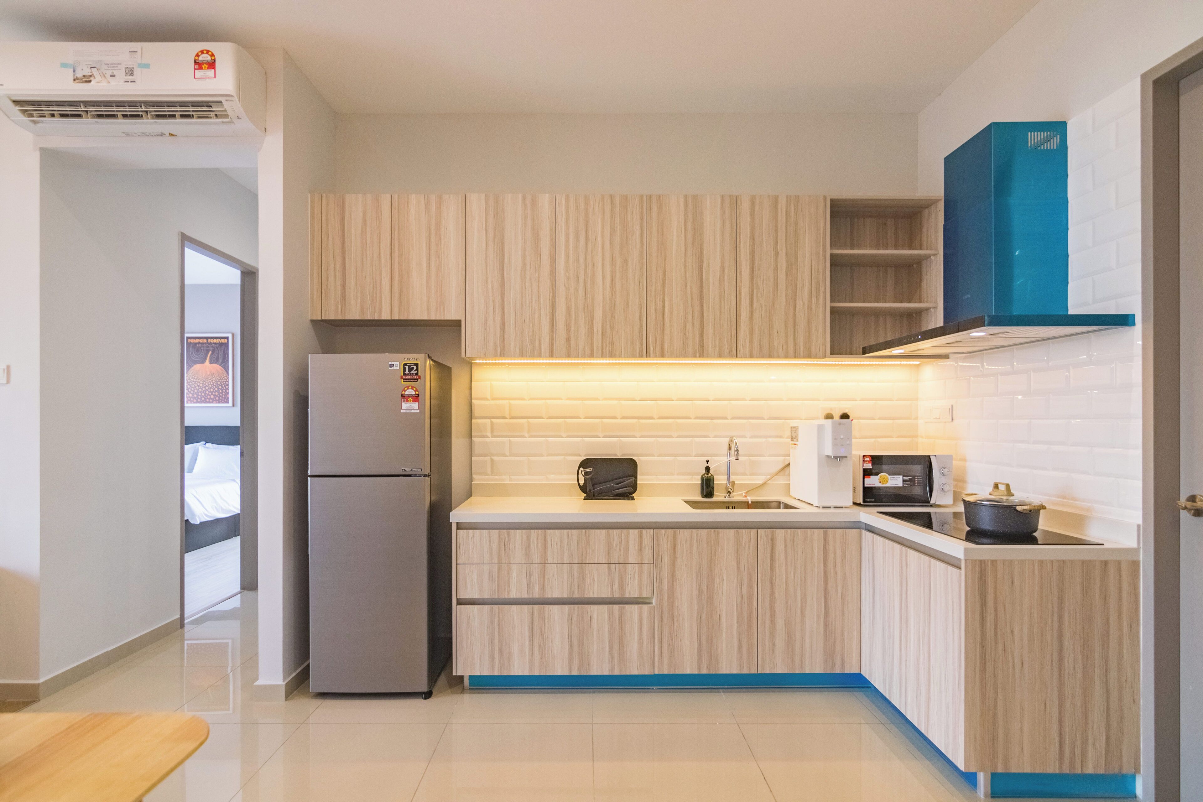 A modern kitchen with light wood cabinets, a built-in oven, a refrigerator, and a blue accent wall.